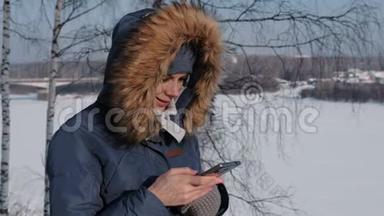 冬天公园里，穿着蓝色羽绒服、带毛衣罩的贴身女人在手机上写短信
